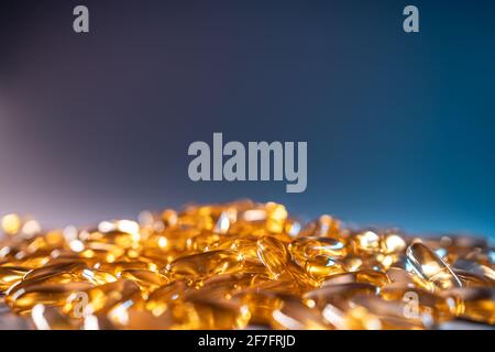 handful of golden fish oil capsules omega 3 vitamins on blue background Stock Photo