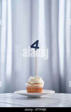 Birthday or anniversary minimalistic greeting card concept. Tasty homemade vanilla cupcake or muffin with creamy topping and number 4 four on white plate and bright background. High quality image Stock Photo