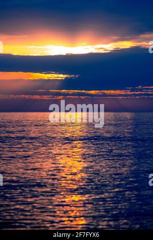 Intense sunrise or sunset at sea with blue clouds and waves illuminated by sun rays. Beautiful landscape saturated in the ocean in summer. Stock Photo