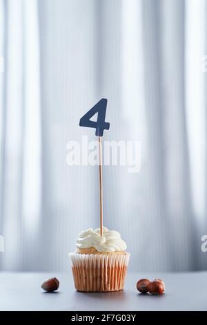 Birthday cupcake or muffin with number 4 four and hazelnuts on table and bright background. Birthday or anniversary greeting card concept. High quality vertical photo Stock Photo