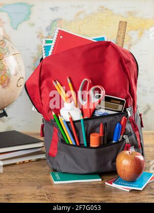 Book bag with an assortment of school supplies on a desk with world map in background Stock Photo