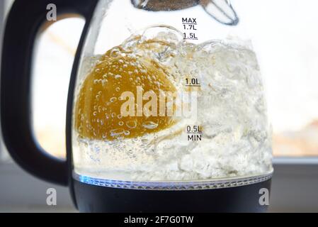 Half a yellow lemon is boiled in a glass electric kettle for descaling Stock Photo