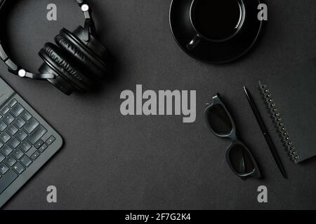 Flat lay top view office desk. Workspace with laptop computer, headphones, coffee cup, paper notebook, pen, glasses on black table. Stock Photo