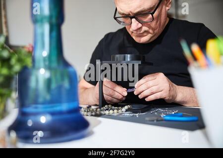 Focused handcrafter inspecting a gemstone with a magnifying glass Stock Photo