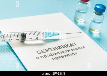 A document for recording vaccinations made in Russia, a syringe and a bottle of vaccine on a blue background. Translated from Russian: Certificate of Stock Photo