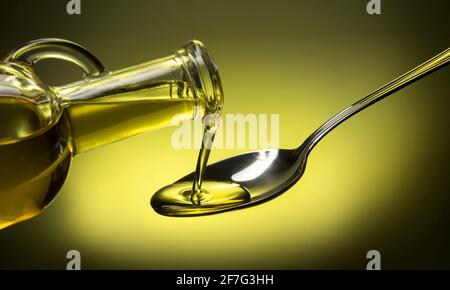bottle pouring oil in a spoon on green background Stock Photo