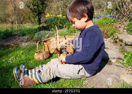 Child young boy sitting in garden after Easter egg hunt looking down at  basket of chocolate Easter eggs in Wales UK Great Britain. KATHY DEWITT Stock Photo
