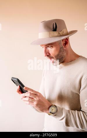 Surprised man in hat using smart phone indoors Stock Photo