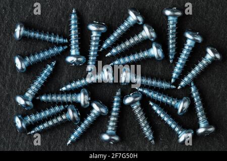 Extreme close up, top down view of aqua blue colored, stainless steel, small, pan head self-tapping screws on black stone surface Stock Photo