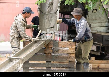 Moscow oblast. Russia. Summer 2019. Pouring concrete slabs. Two workers prepare a tray for draining concrete from a concrete mixer. Stock Photo