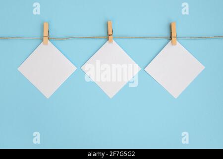 Empty paper sheet for notes, frames that hang on a rope with clothespin and isolated on blue background. White blank with empty space for text. Stock Photo