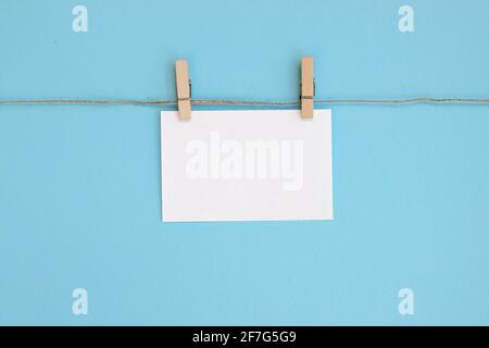 Empty paper sheet for notes, frames that hang on a rope with clothespin and isolated on blue background. White blank with empty space for text. Stock Photo