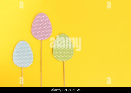 Multicolored Easter eggs on wooden sticks, isolated yellow background. Easter holiday greeting card with copy space. Stock Photo