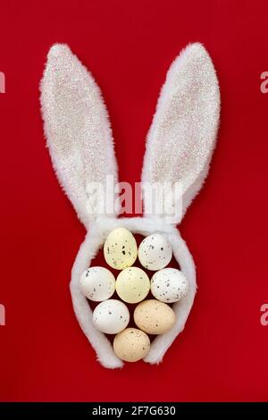 Fluffy bunny ears with colored Easter eggs isolated on red background, top view, flat lay. Stock Photo