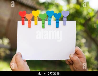children's hands hold a sheet of white paper with colorful pins in the shape of a heart in colors of rainbow. Place for advertisements, invitations, a Stock Photo