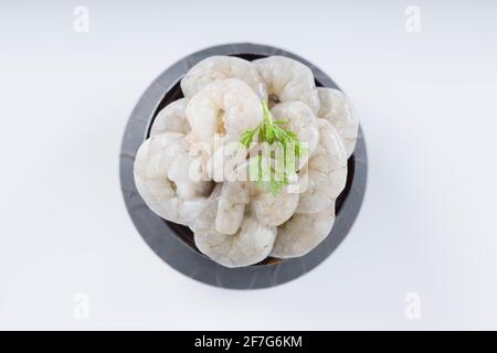 Raw peeled prawns or shrimp arranged in a black ceramic small pot and garnished with coriander leaf which is ready to cook ,placed on a white textured Stock Photo