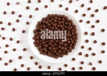 Plate of Chocolate cornflakes isolated on a white background. Dry breakfast chocolate flavored balls. Top view Stock Photo