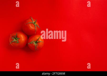 red tomato with green stalk, three fresh tomatoes on red background Stock Photo