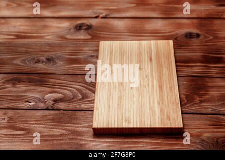Cutting board made of bamboo on a brown wooden background. Top view. Stock Photo