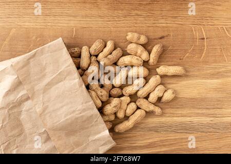 Peanuts in shell on wooden table, food composition with small paper bag. Beer snacks. Healthy food concept. Space for text. Stock Photo