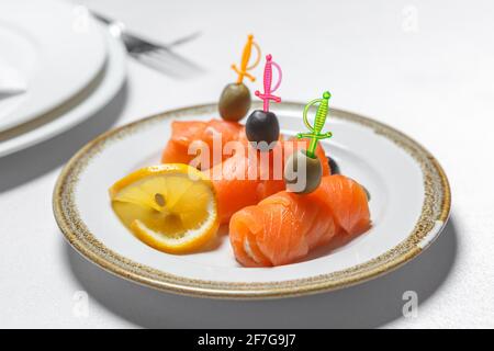 Red fish on skewers with olives and lemon is on a plate. The concept of festive table setting. Stock Photo