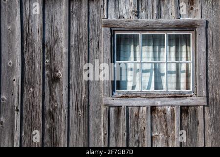 An old settler home in Lucan, Ontario, with worn wooden planks and a cute window with plaid curtains, photographed February 2021.