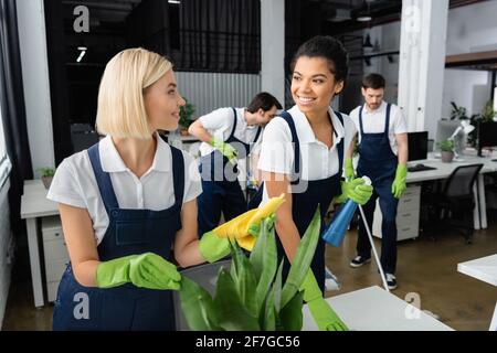 Interracial cleaners smiling at each other in office Stock Photo