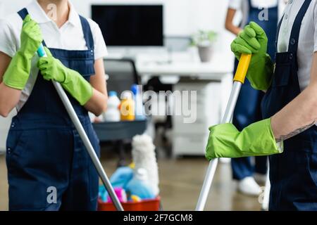 Cropped view of cleaners in rubber globes holding mops in office Stock Photo