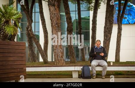 young bald adult sitting after a business meeting holding his tablet device and having a coffee to go while on his social media.real people daily work Stock Photo