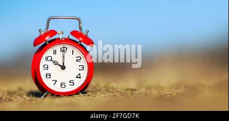 Retro red alarm clock in the grass, save or manage time concept. Web banner with copy space. Stock Photo