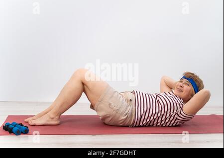 Happy old woman doing abs exercises on a sports mat. Elderly lady doing fitness. Stock Photo