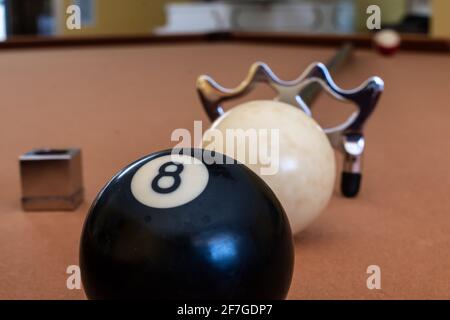 A billiards bridge aid, white ball, eight ball and cue chalk line up on a gold felt pool table, Toronto, Ontario Canada. Stock Photo