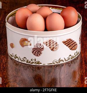 A round tin box in which pastries are usually stored was filled with eggs, on a wooden table Stock Photo