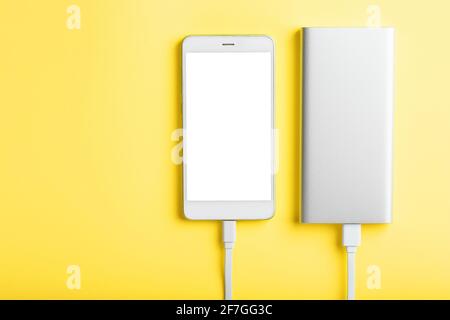 Power Bank charges a smartphone on a yellow background. Universal external battery for gadgets. Free space and minimalistic composition. View from abo Stock Photo