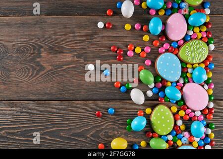 Dark wooden background with chocolate round candies and colorful eggs made from gingerbread, lying accurately on right side. Flat lay, top view, copy space Stock Photo