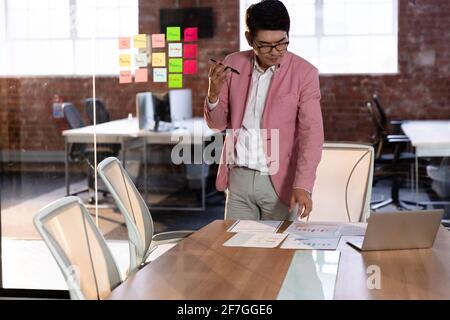 Stylish asian businessman having conversation standing by desk using smartphone Stock Photo