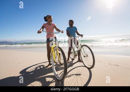 Happy african american couple on beach riding bicycle Stock Photo