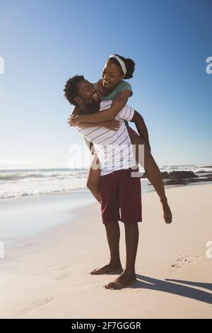 Happy african american couple on the beach piggybacking looking at each other Stock Photo