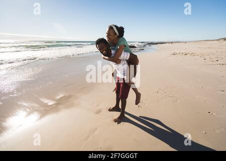 Happy african american couple on the beach piggybacking Stock Photo