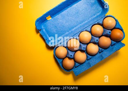 Fresh eggs in and out of blue carton box isolated on yellow background Stock Photo