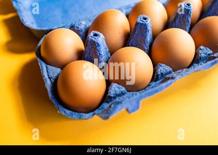 Fresh eggs in and out of blue carton box isolated on yellow background Stock Photo
