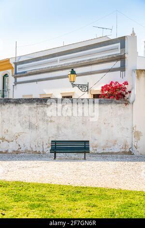 Wooden bench on the whitewashed wall background with traditional Portuguese architecture behind in Faro, Algarve, Portugal Stock Photo
