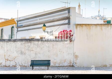 Wooden bench on the whitewashed wall background with traditional Portuguese architecture behind in Faro, Algarve, Portugal Stock Photo