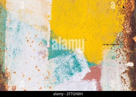 Old rusty sheet of industrial iron with random brushstrokes of white, blue, yellow and pink paint in a full frame background texture or design templat Stock Photo