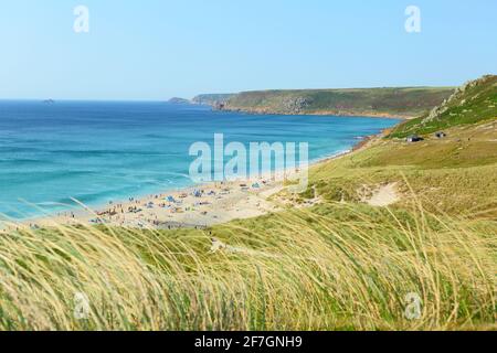 People enjoying a sunny summers day on the beach in Sennen Cove, Cornwall, England, UK showing the sandy beach and blue sea under a blue sky. Stock Photo