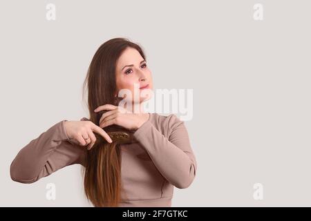 young beautiful woman combing her long straight hair with a comb on a light background Stock Photo