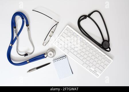 Two stethoscopes on the table in the doctor's office. Top view of desk table with computer keyboard, glasses and notebook with pen. Designer's blank Stock Photo