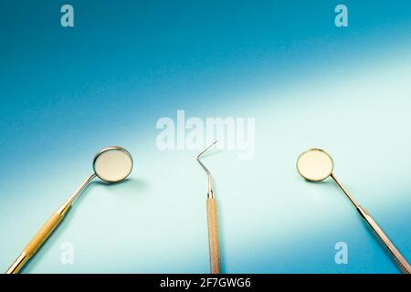 Dentist tools: mirror, dental explorer and tweezers lying on blue background in light ray. Stock Photo