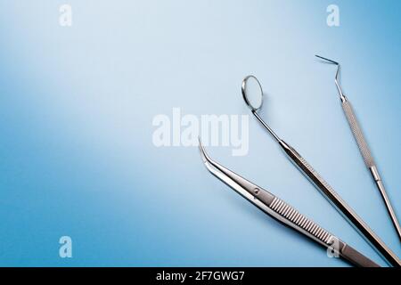 Dentist tools: mirror, dental probe and tweezers lying in right on blue gradient background. Stock Photo