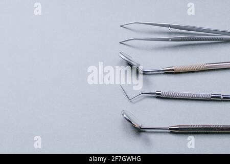Dentist tools: two mirrors, dental probe and tweezers lying on gray background on right side. Stock Photo